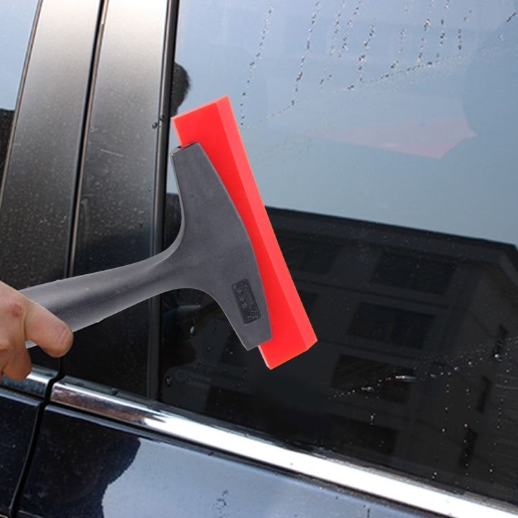 Handheld window film scraper using a black handle and red squeegee blade on glass