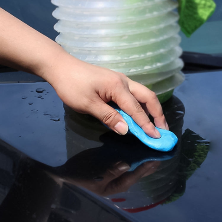 Hand using blue clay bar on dark car paint to lift dirt