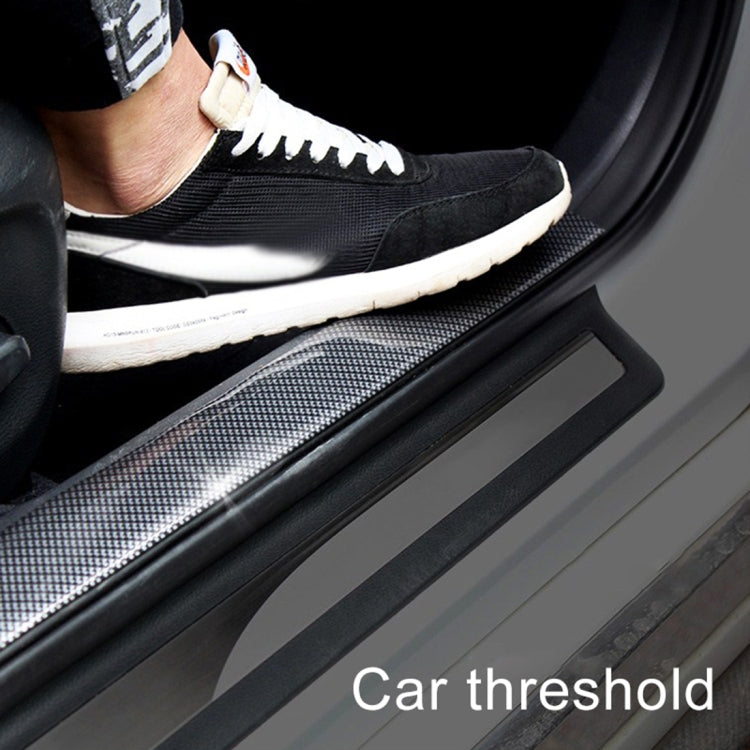 Black carbon-fiber-look car threshold trim strip on door sill, near a shoe