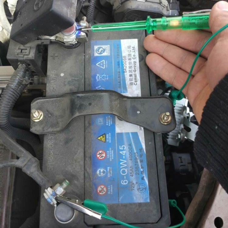 Hand holding green voltage detector pen with cable on vehicle electrical panel