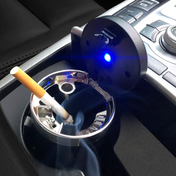 Portable car ashtray with open red lid, blue light glow, and cigarette resting inside.