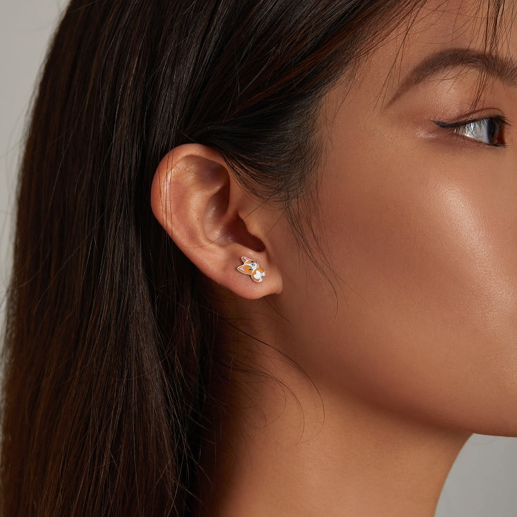 Woman wearing corgi ear stud earrings, sterling silver with orange and white enamel