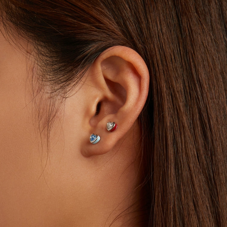 Silver heart stud earrings with blue and red zircon stones on an ear