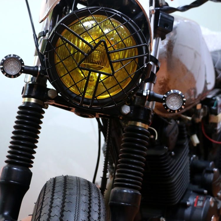 Installed motorcycle headlight grill guard: black round wire mesh with arrowhead center
