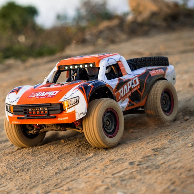 Orange-and-white brushless RC pickup truck side view on dirt with large off-road tires