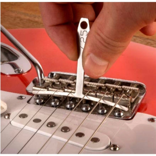 Metal guitar fret measuring ruler being used on fretboard near strings and bridge