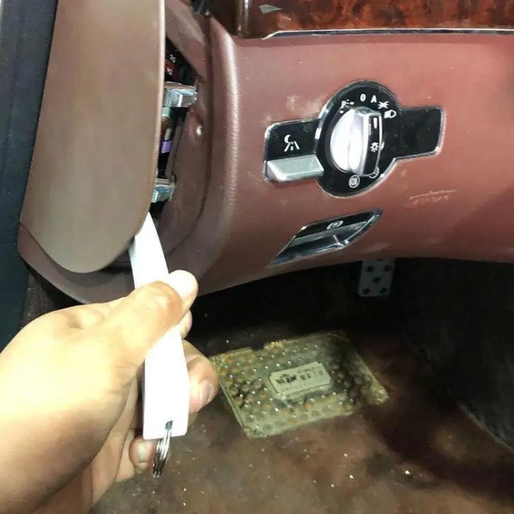 White trim removal tool held by hand, prying at an interior panel opening