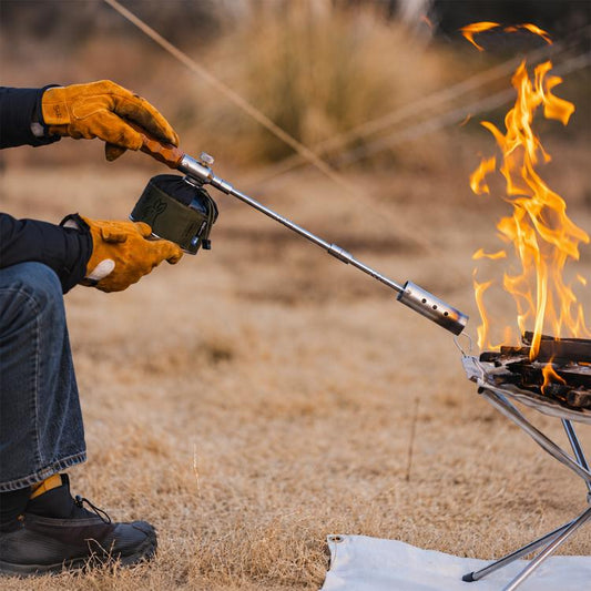 Portable camping blowtorch with extended metal nozzle, producing an outdoor flame