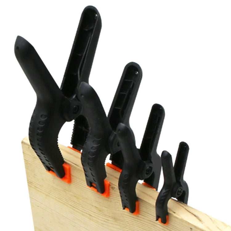 Set of 5 black spring clamps with orange release tabs for holding backdrops on wood