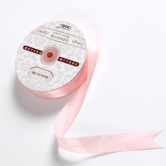 Pink satin packaging ribbon roll with printed English letters, visible ribbon tail