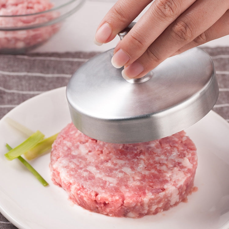Stainless hamburger meat press with round lid, pressing a raw pink patty on a plate