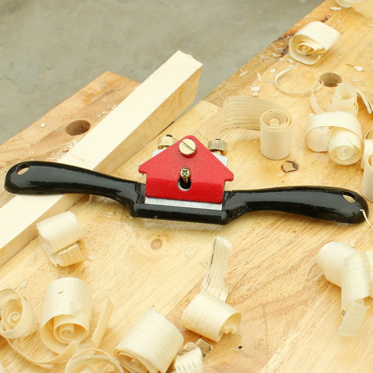 Hand wood planer on plywood with curled shavings and red cutter housing