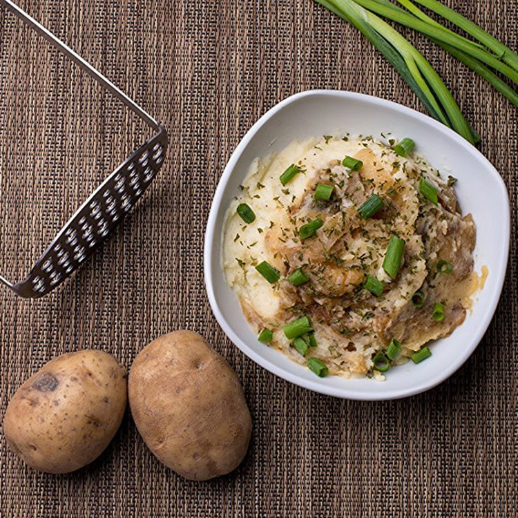 Manual stainless steel ricer tool with black handle beside a mashed potato bowl