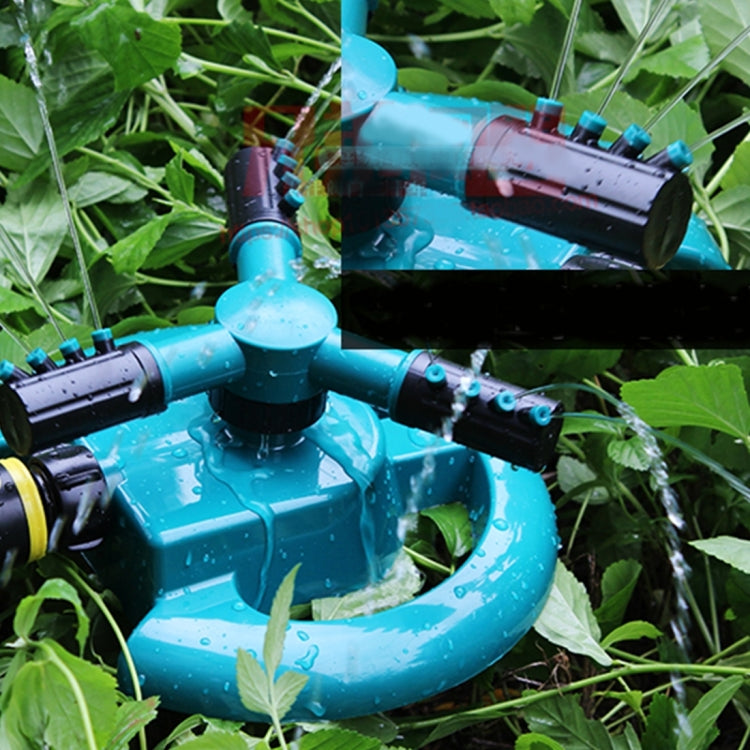 Teal rotary sprinkler in foliage with black nozzle arms and water spray