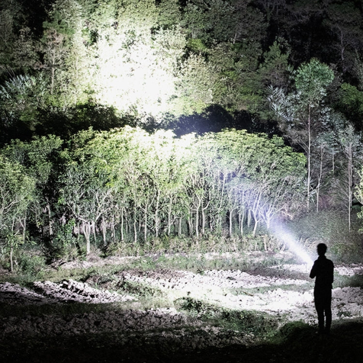 Rechargeable LED searchlight flashlight casting a bright beam over an outdoor wooded area