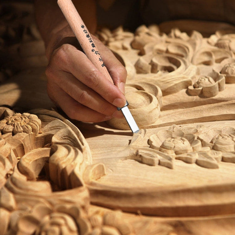 Hand using a wood carving chisel with wooden handle on carved wooden block