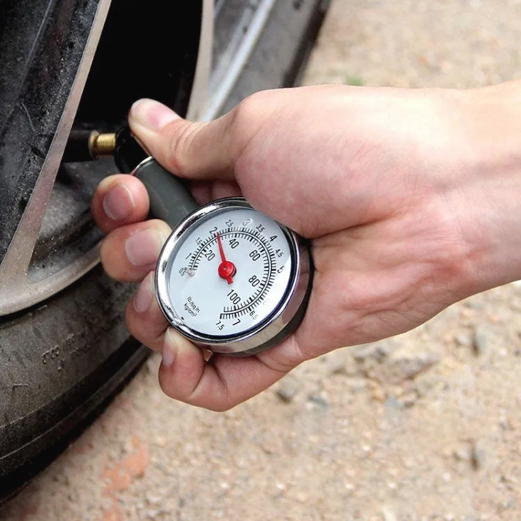 Handheld tire pressure gauge connected to a car valve stem, showing dial readout