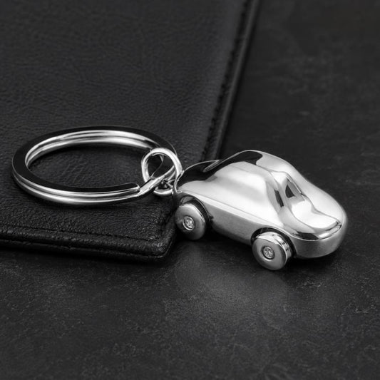 Car-shaped metal key chain with split ring and small wheels on dark surface