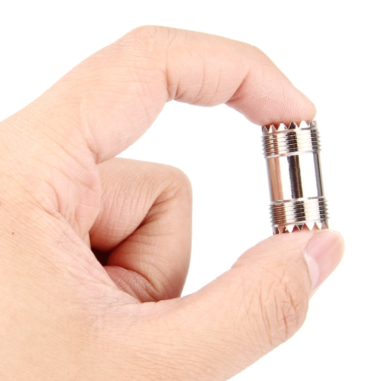 UHF female-to-female RF connector held in hand, silver threaded body with female sockets