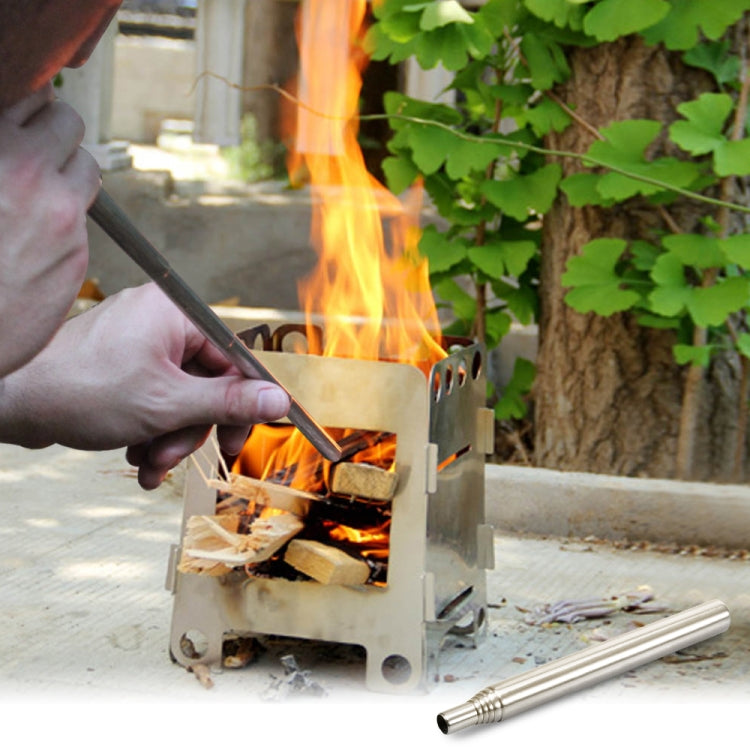 Stainless steel fire blower tool placed beside burning logs for outdoor cooking