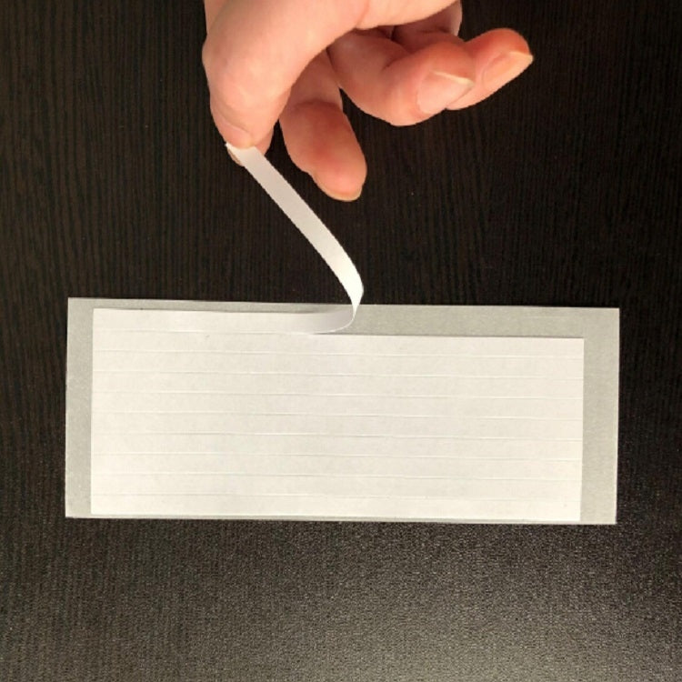 Blank white label strip for gift wrapping, held above a dark surface.