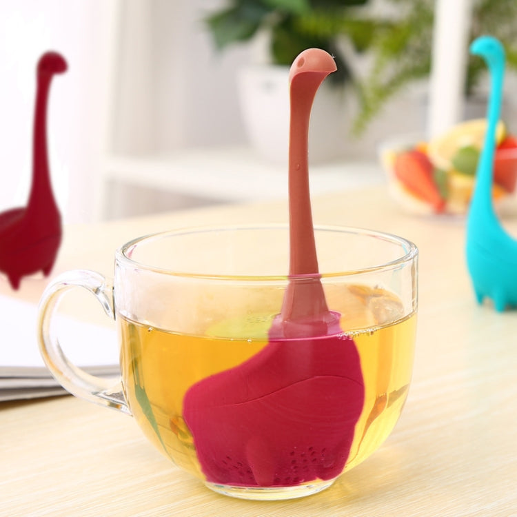 Red dinosaur tea infuser strainer in a glass teacup with hot tea.