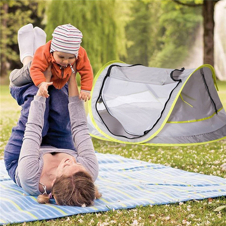 Portable baby mosquito net tent with lime-green trim beside child on outdoor blanket