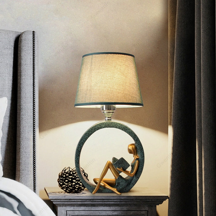 Bedside table lamp with beige fabric shade and circular figurine base, close view.