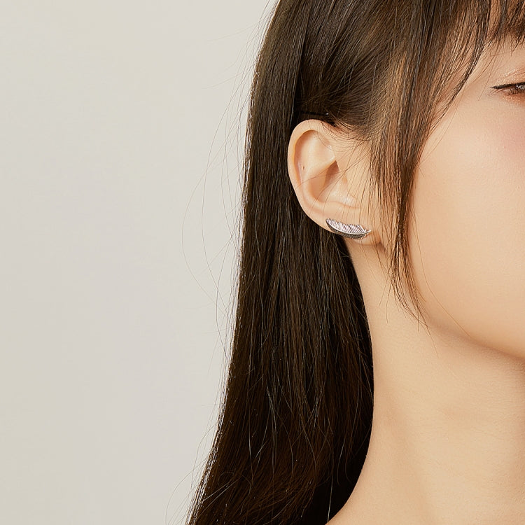 Silver ribbed feather earrings worn on ear, side profile view