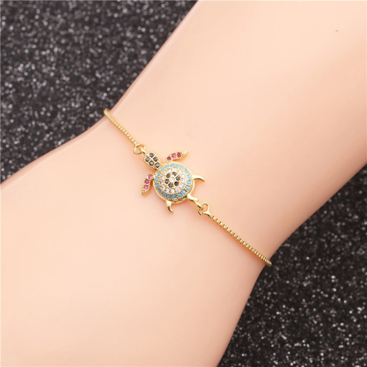 Gold-tone turtle charm bracelet on wrist with blue center and pink and black stone accents