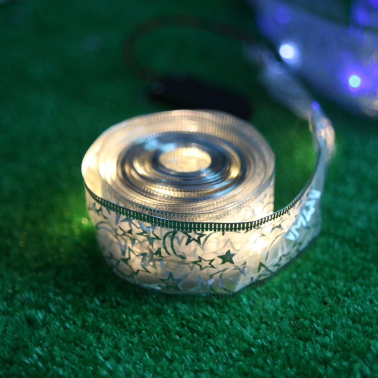 LED string light coil close-up with star-print purple-silver ribbon on green turf