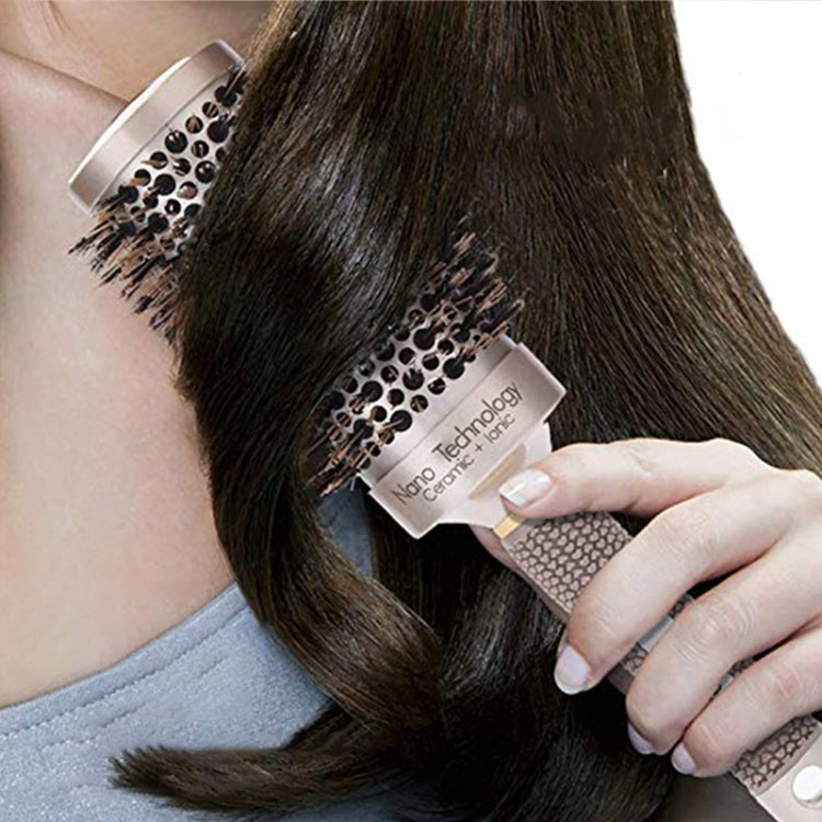 Round hair styling brush with black bristles and beige-gold handle, brushing dark hair
