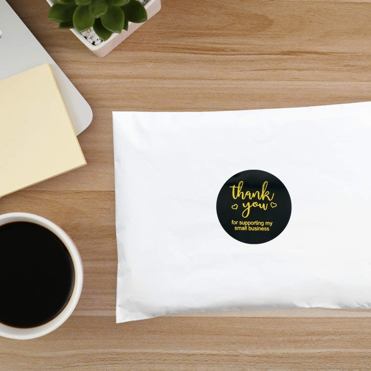 Small black round thank you sticker with gold foil text on a white envelope