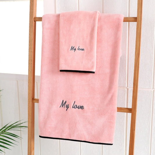 Pink bath towel with “My love” embroidery and dark border, folded on a wooden rack