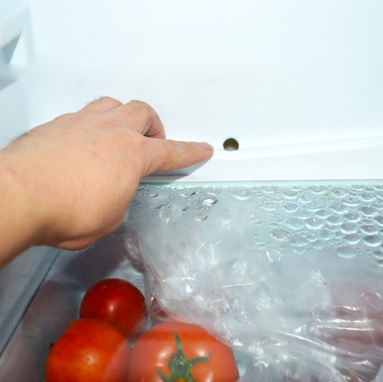 Hand inserting flexible drain cleaner into refrigerator drain hole with nozzle near opening