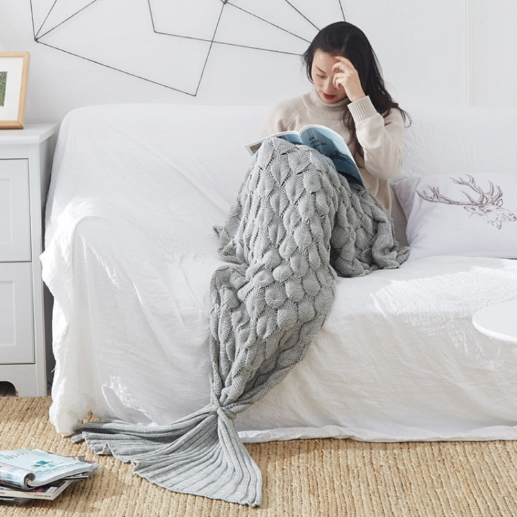 Gray knitted mermaid-tail blanket, folded with fin detail, on bed