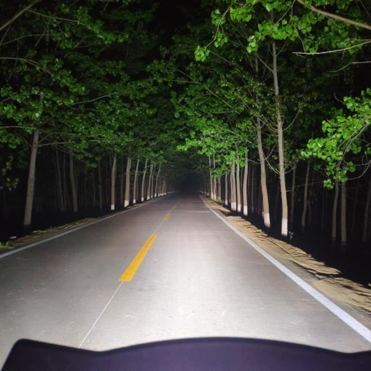 Wide white LED beam from the motorcycle spotlight illuminating a dark road