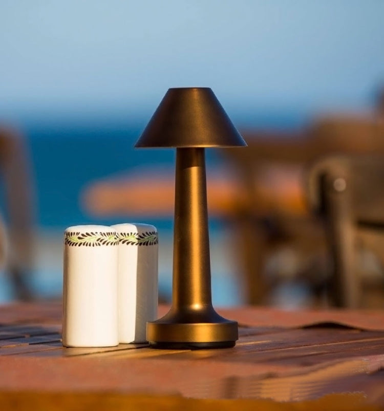 Lit golden LED touch table lamp with conical shade on wooden surface