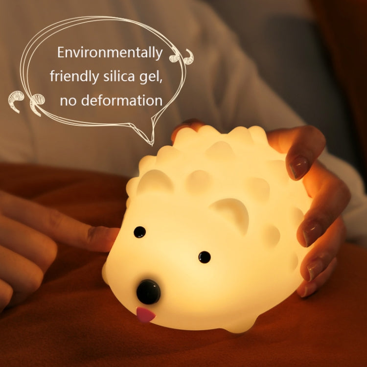Hedgehog night light with warm glow held in hands over a couch