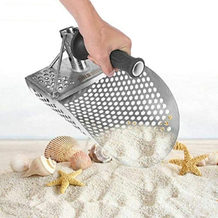 Gold panning sand shovel in hand with perforated scoop over sand and shells.