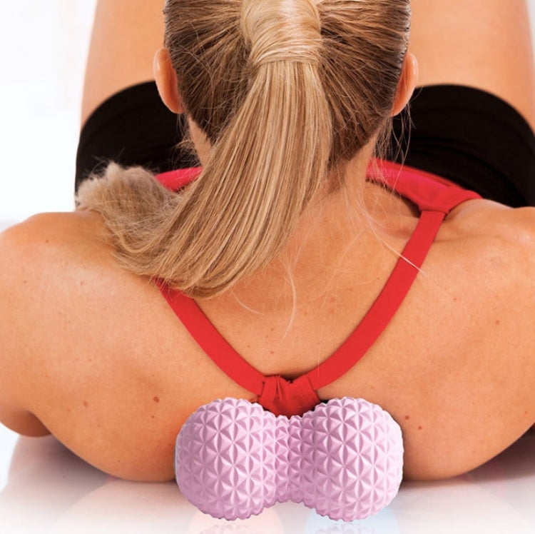 Pink textured massage peanut ball placed under shoulders for massage.