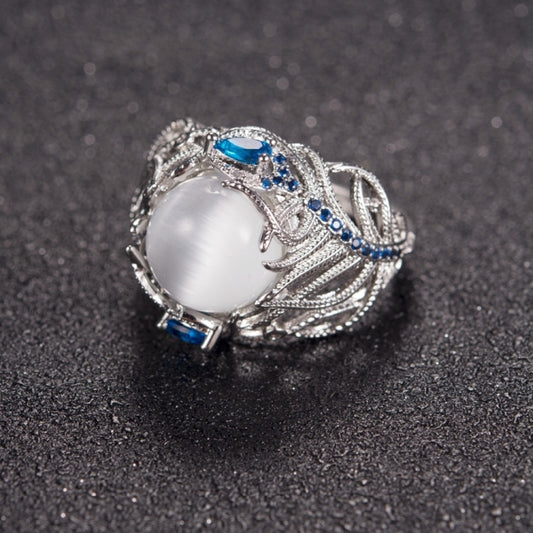 Silver-tone ring with oval white cabochon and blue gemstone accents on carved band