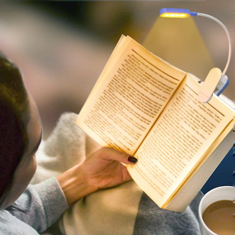 Blue mini clip desk lamp clipped to an open book, illuminating reading pages