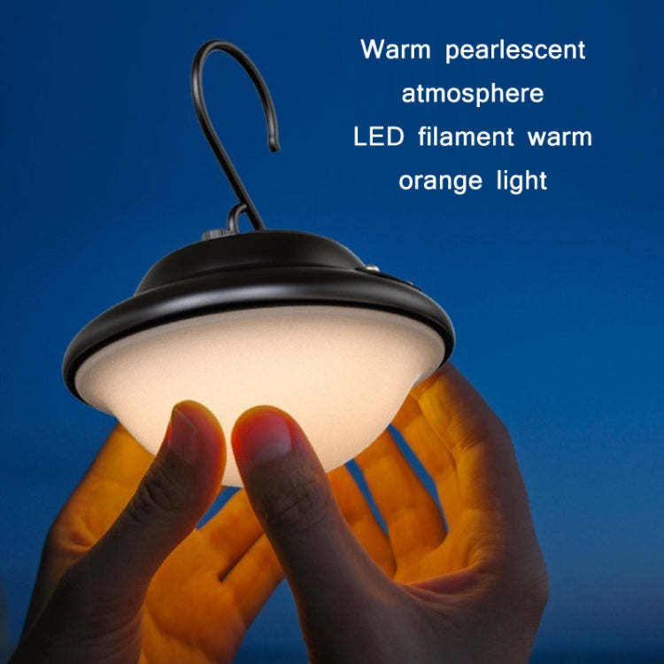 Portable hanging camping light emitting warm orange glow held by hands