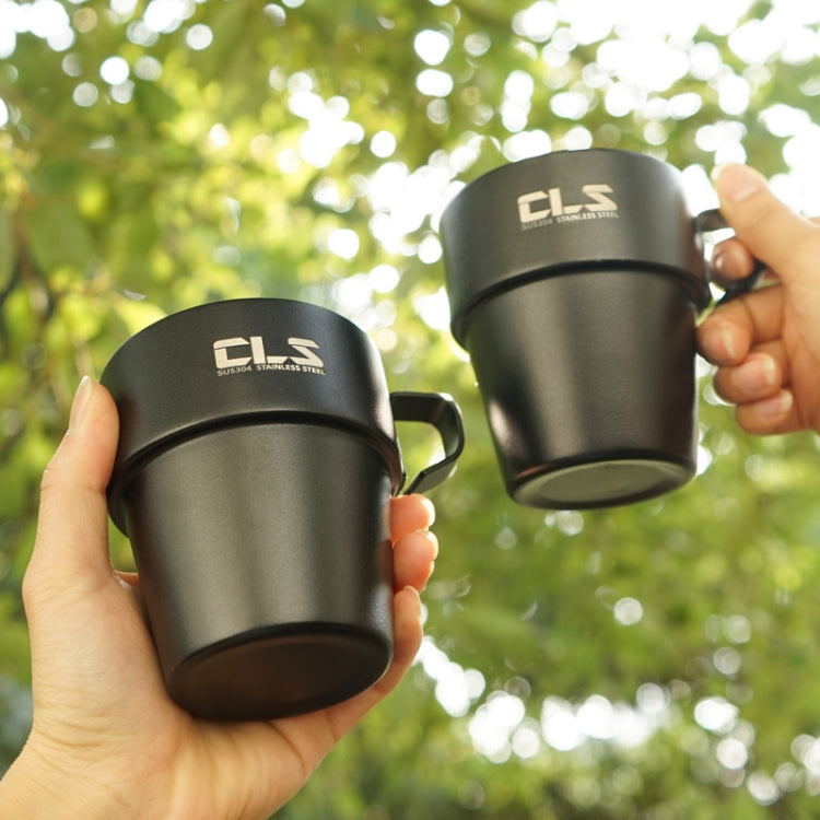 Two black stainless camping cups with handles held in hands outdoors