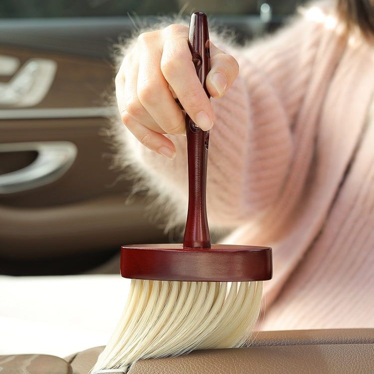 Car dust brush with dark wood handle and round beige bristle top held above seat