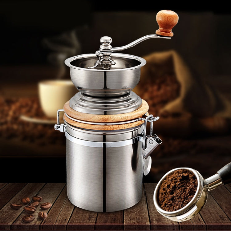 Stainless steel hand coffee grinder with wooden crank knob and metal scoop of grounds