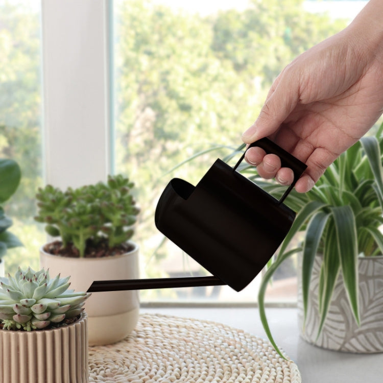 Hand holding black stainless steel watering can with long spout and square handle