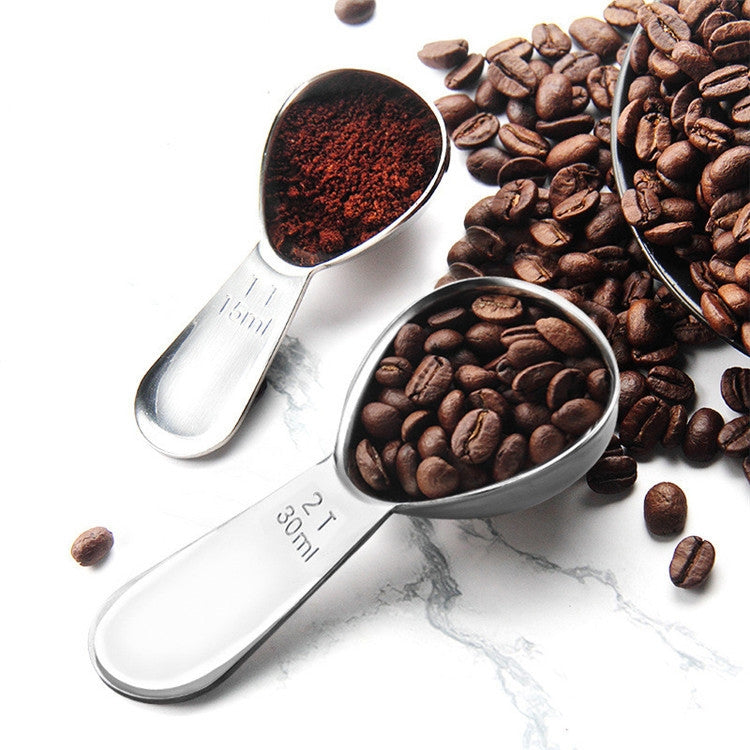 Small stainless steel coffee measuring spoon pair with dark coffee grounds in the cups