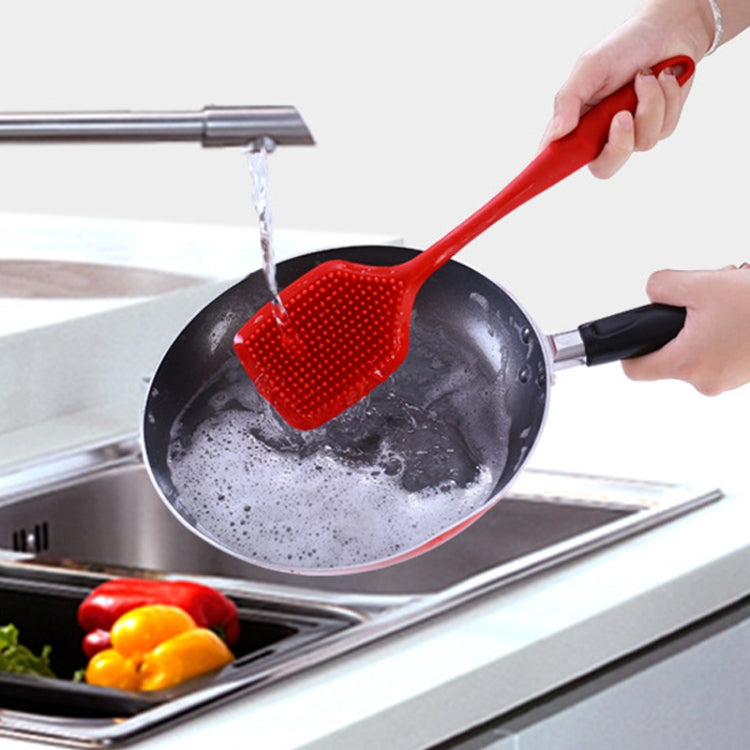 Red silicone scrubbing brush cleaning a nonstick pan with suds
